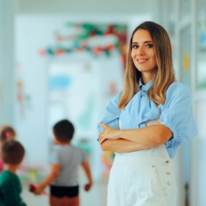 A bölcsőde folyosóján egy fiatal nő karba tett kézzel mosolyogva néz a kamerába