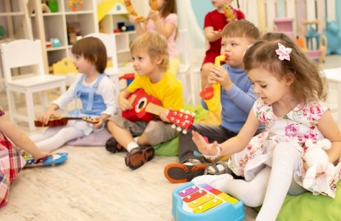 Kisgyermekek ülnek a szőnyegen a csoportszobában. Mindenki különféle hangszerekkel játszik. Csörgővel, xilofonnal, kis gitárral, fújós hangszerekkel zenélnek
