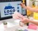 A bölcsőde logója kiemelt kép - a képen egy pantone színskálát tart egy női kéz, a háttérben monitoron egy hegyet ábrázoló logo terv