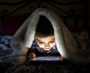 Média a kisgyermekek életében illusztráció - egy kisgyerek a sötétben paplan alatt nézi a telefonját