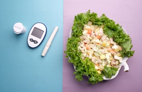 A kép baloldalán a vércukorméréshez használt eszközök, egy doboz gyógyszer látható, jobb oldalon pedig saláta egy tányéron.