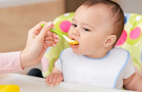 A kiemelt képen egy kisbaba ül etetőszékben, kanállal etetik.