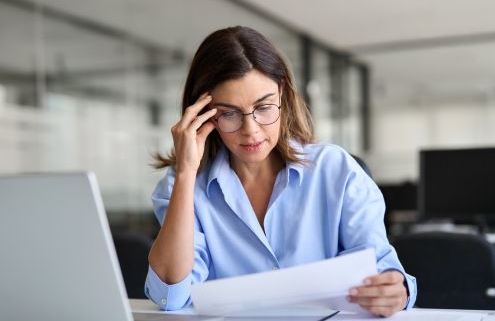 Egy középkorú hölgy a laptop előtt ülve gondterhelten iratokat nézeget.