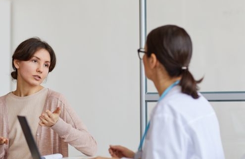 A képen két nő beszélget, az egyik előtt laptop, a másik széttett karokkal magyaráz