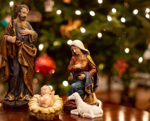 Kerámia Betlehem Máriával, Józseffel és a kis Jézussal. A háttérben karácsonyi fények