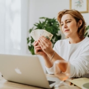 Óvodában foglalkoztatottaknak járó illetmények 2026-ban - egy középkorú hölgy pénzt számolgat a laptopja előtt ülve