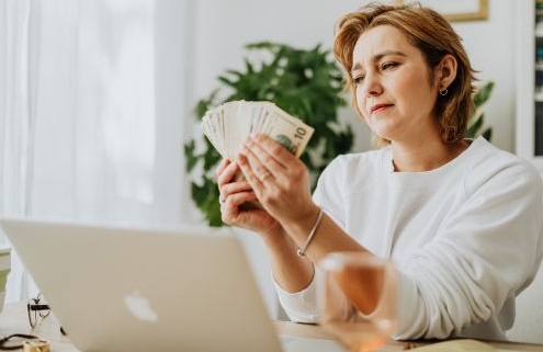 Óvodában foglalkoztatottaknak járó illetmények 2026-ban - egy középkorú hölgy pénzt számolgat a laptopja előtt ülve