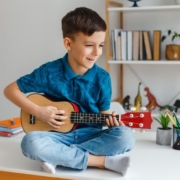 Tehetséges gyermek a családban - egy kisfiú az asztalon ül, ukulelézik.