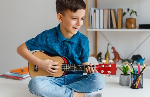 Tehetséges gyermek a családban - egy kisfiú az asztalon ül, ukulelézik.