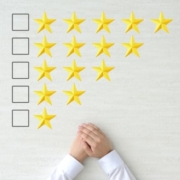 Teljesítményértékelés. A képen fentről lefelé 5 sorban csillagokat látunk - a felső sorban 5 csillag, az alsóban 2, csökkenő sorrendben. A sorok elején rubrika, ahol bejelölhető hogy hány csillagra értékeljük a teljesítményt. Az alsó sor alatt egy ember kezei láthatók ahogy idegesen tördeli őket: vajon milyen értékelést kap?