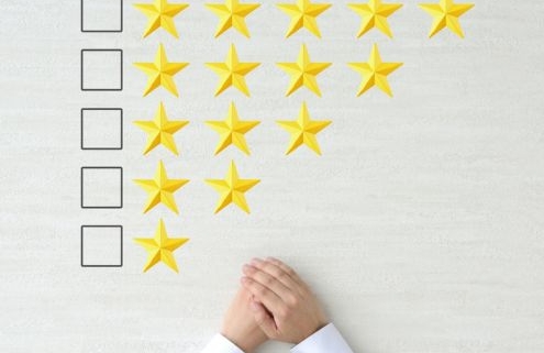 Teljesítményértékelés. A képen fentről lefelé 5 sorban csillagokat látunk - a felső sorban 5 csillag, az alsóban 2, csökkenő sorrendben. A sorok elején rubrika, ahol bejelölhető hogy hány csillagra értékeljük a teljesítményt. Az alsó sor alatt egy ember kezei láthatók ahogy idegesen tördeli őket: vajon milyen értékelést kap?