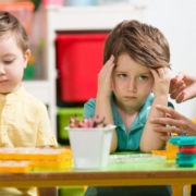 Dühös kisfiú ül az óvodai asztalnál a társa mellett. Egy óvónő simogatja a karját, próbálja megnyugtatni