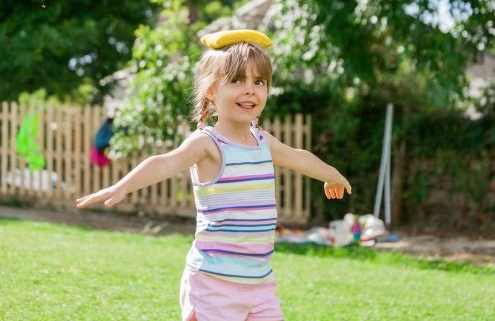 Egy kislány a szabadban babzsákot egyensúlyoz a fején