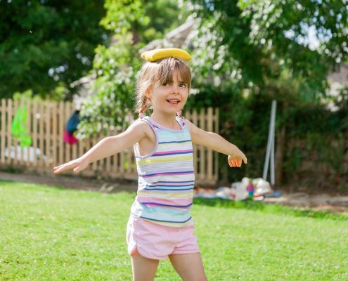 Egy kislány a szabadban babzsákot egyensúlyoz a fején