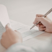 A kiemelt képen valaki aláír egy hivatalos iratot tollal a kezében