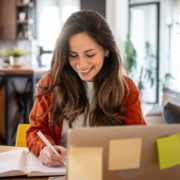 Hogyan készüljünk a minősítési eljárásra Hogyan készüljünk a minősítési eljárásra - mosolygós nő dolgozik egy laptop mögött