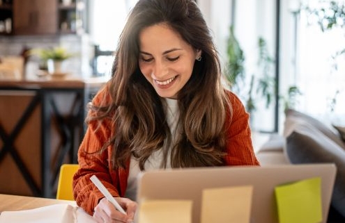 Hogyan készüljünk a minősítési eljárásra - mosolygós nő dolgozik egy laptop mögött