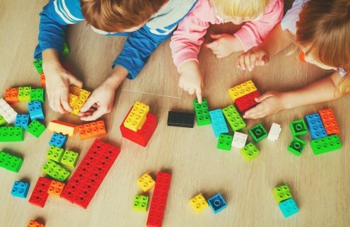 A képen három kisgyermek legózik hason fekve