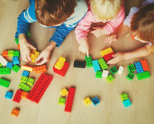 A képen három kisgyermek legózik hason fekve