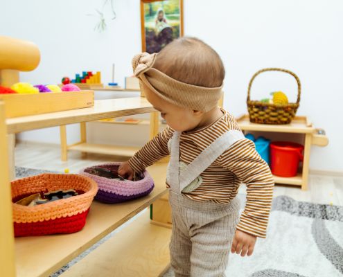 A képen egy fejpántos kislány játszik szövött kosarakban lévő játékokkal