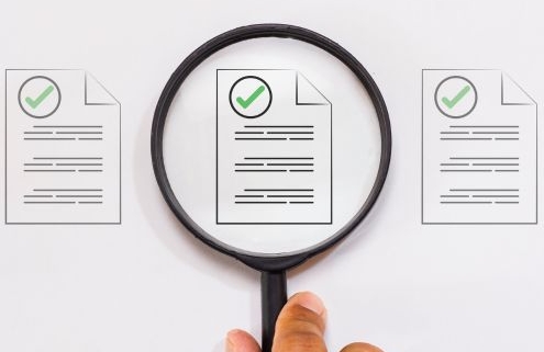 Egy kéz nagyítót tart, amely 3 egyforma dokumentum ikon közül a középsőt vizsgálja