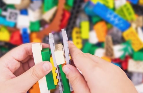 Egy kisgyermek kezét látjuk aki LEGO-ból épít valamit. A háttérben is LEGO kockák vannak