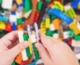 Egy kisgyermek kezét látjuk aki LEGO-ból épít valamit. A háttérben is LEGO kockák vannak