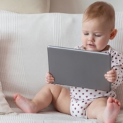 Pár hónapos csecsemő a kanapén ülve tabletet néz