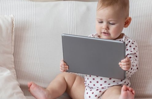 Pár hónapos csecsemő a kanapén ülve tabletet néz