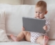 Pár hónapos csecsemő a kanapén ülve tabletet néz